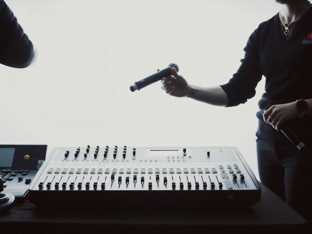 A crew member passing a handheld microphone across a mixing desk